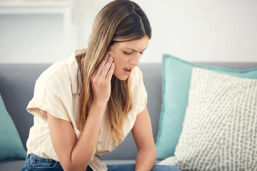 Woman experiencing jaw pain and discomfort, possibly from TMJ or jaw clicking may benefit from Strategic Hypnotherapy offered by MindShift Mentors.