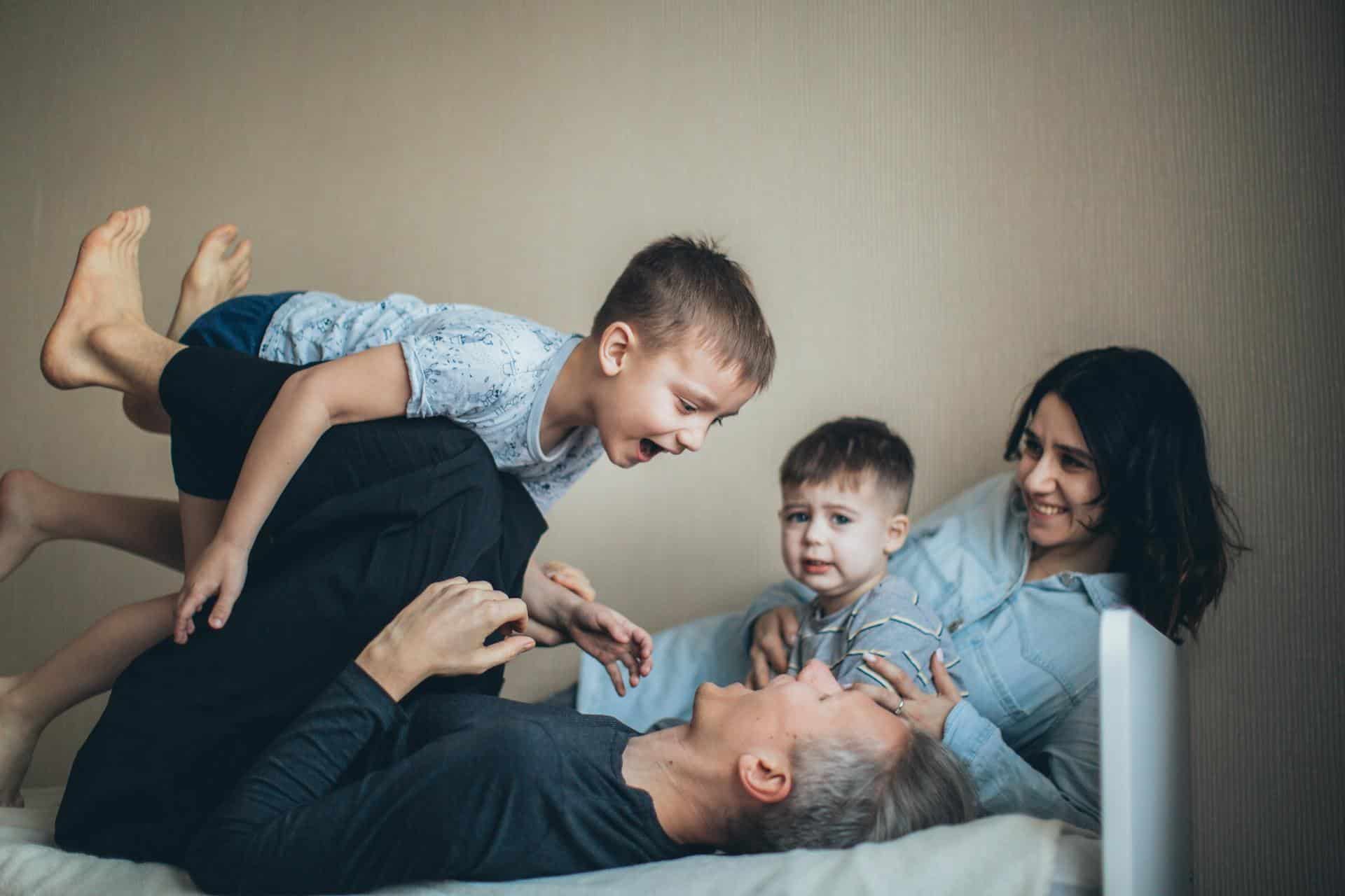 Happy family playing together on a bed, with two young brothers interacting playfully with their parents.