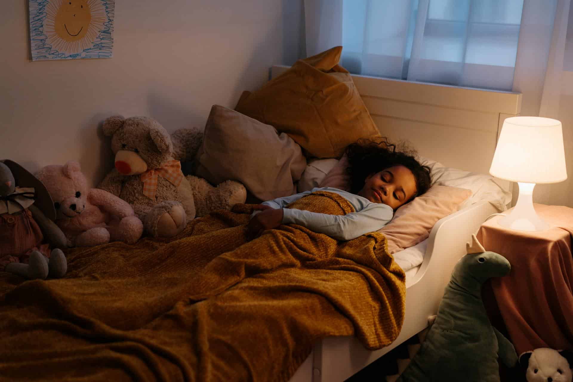 Young child peacefully sleeping in bed surrounded by soft toys, illustrating a calm bedtime routine that supports better sleep for kids with ADHD.