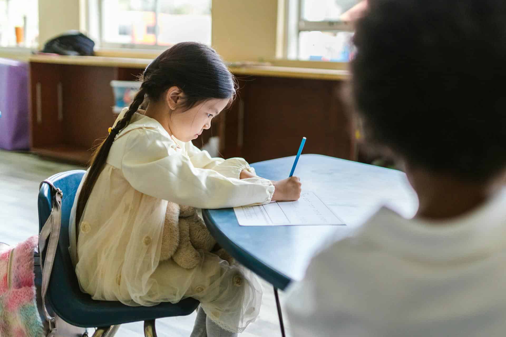 Young girl concentrating on her homework at a classroom desk, practicing focus as part of an ADHD friendly homework routine.
