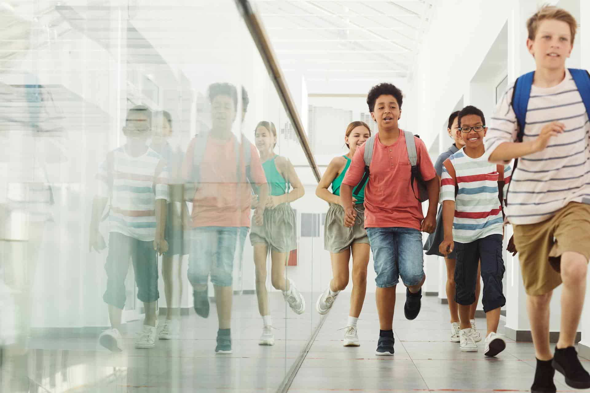 Group of school children with backpacks running and smiling after class in a hallway