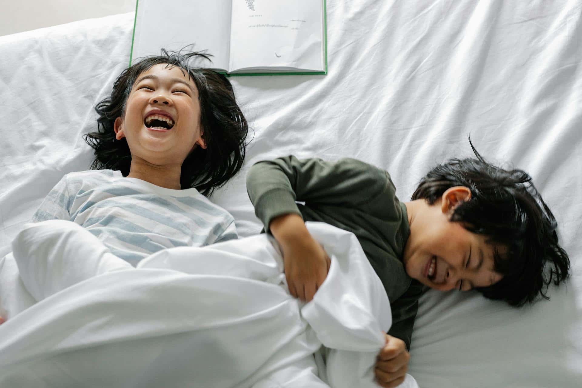 Two kids laughing and playing on a bed in the morning, showing a positive and joyful start to the day for children with ADHD.