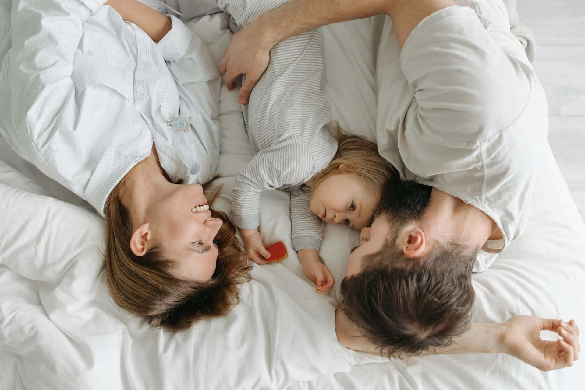 Mother, father, and young child lying together in bed, sharing a calm and intimate morning moment demonstrating the importance of family connection in ADHD routines.