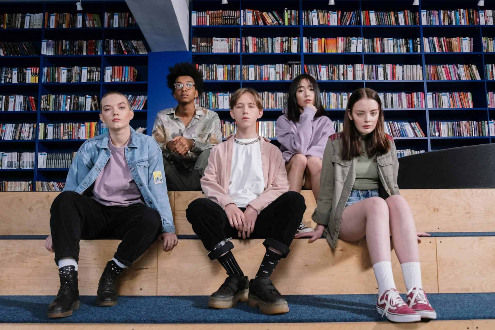 Group of diverse teenagers sitting quietly in a library, appearing thoughtful or serious