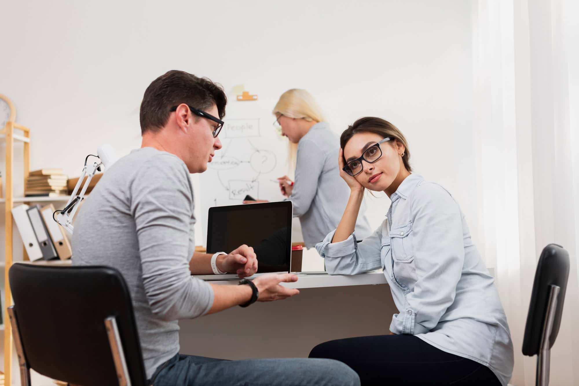Woman looking frustrated during a workplace discussion while a colleague explains something, representing communication and organizational challenges faced by adults with dyspraxia.