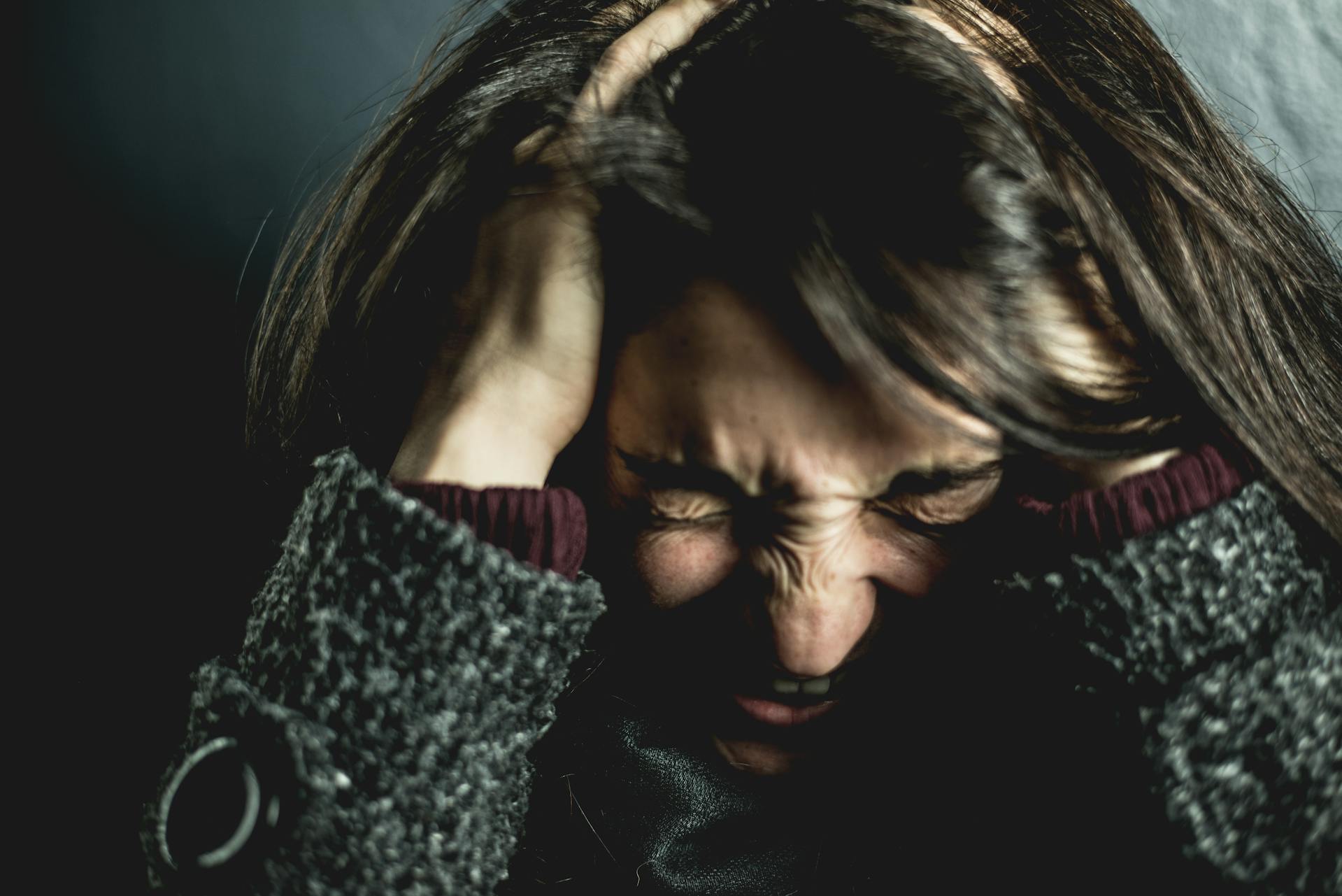 A person sits on the floor with their head buried in their knees and hands covering their head, illustrating an emotional breakdown or intense anxiety and stress response.