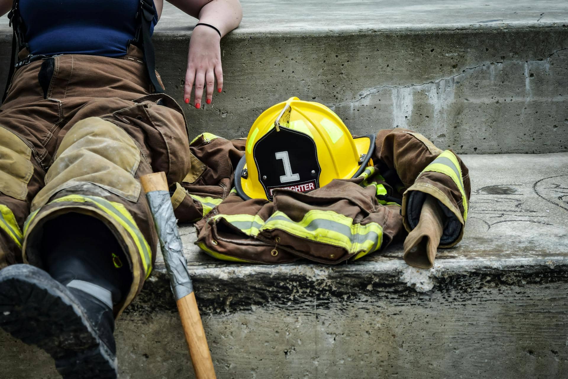 A first responder resting on concrete steps with turnout gear, helmet, and axe laid beside them, symbolising emotional compartmentalisation, exhaustion and the weight of the job. Compartmentalisation