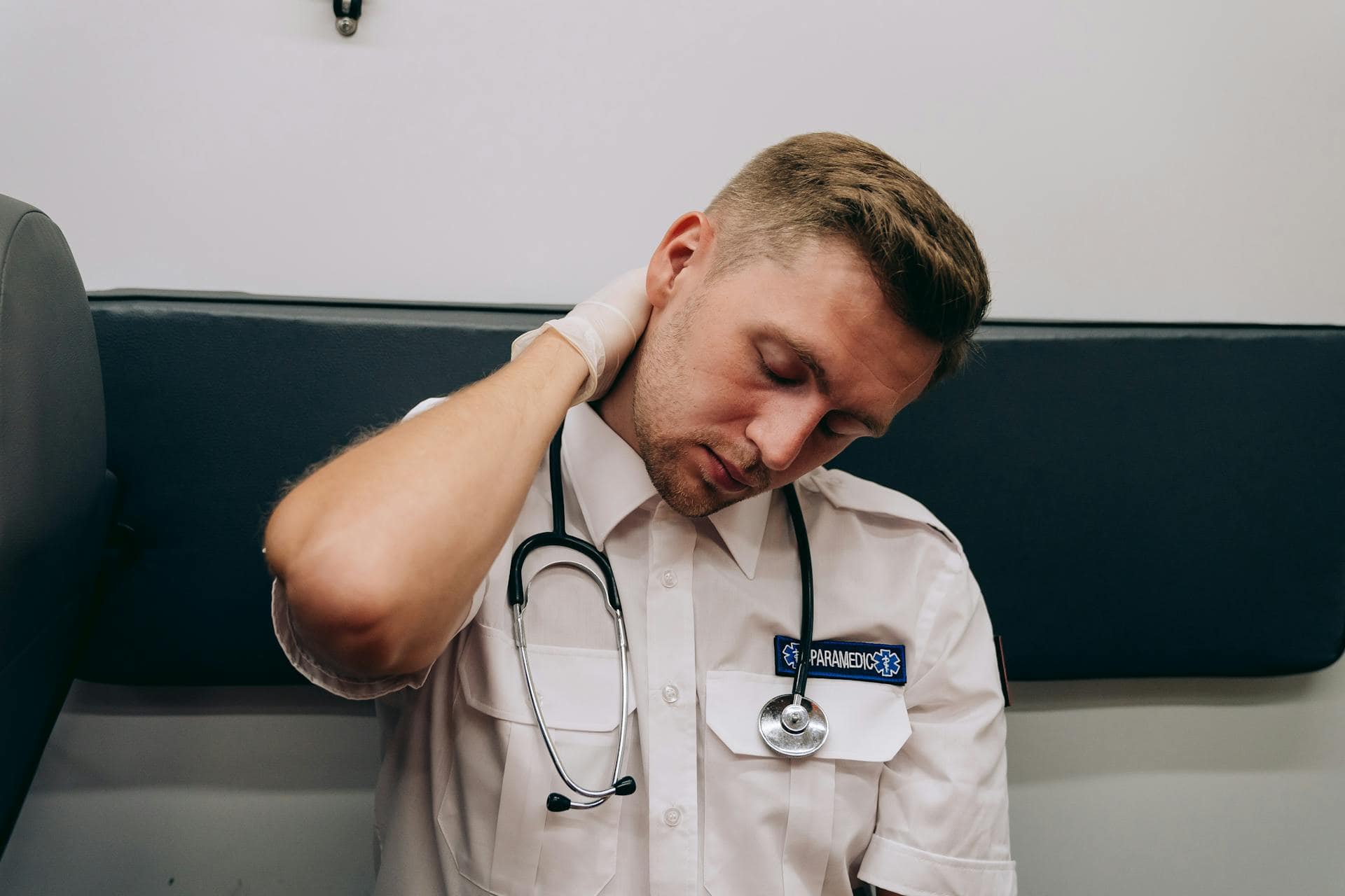 Exhausted paramedic rubbing neck in an ambulance, feeling stressed after long shifts