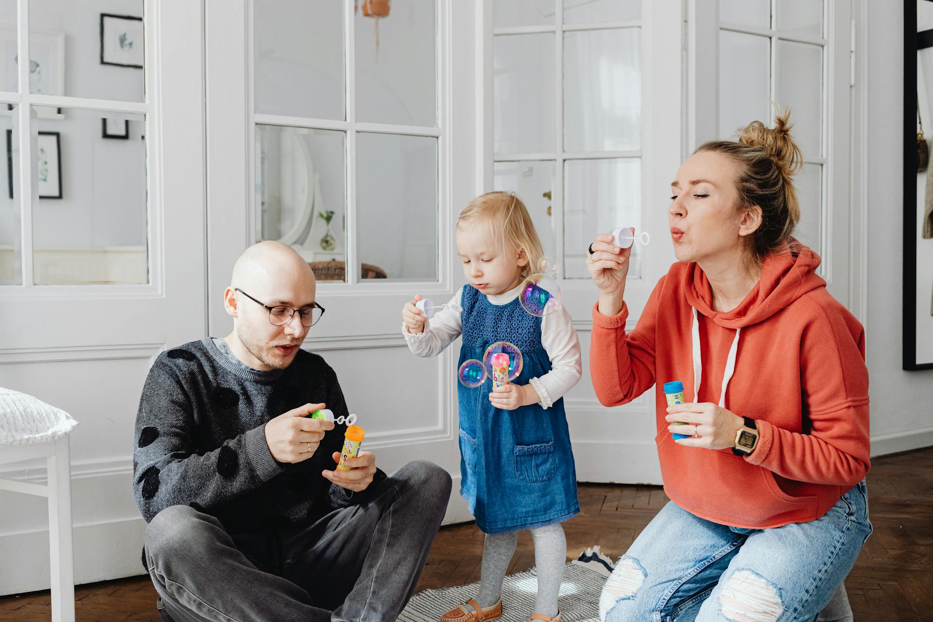 Happy family playing with bubbles indoors father, mother, and young daughter enjoying quality time together at home.