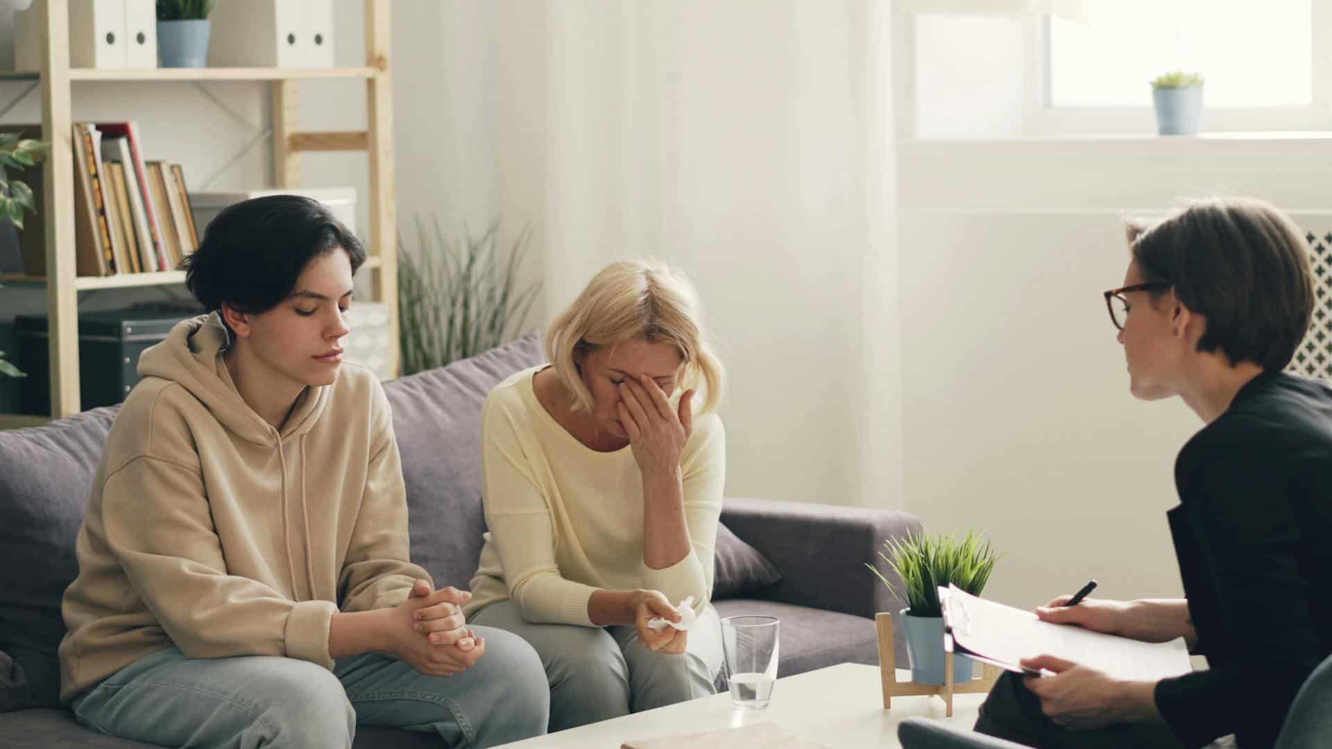 Teen and parent in an emotional family therapy session with a counselor in a calm office setting