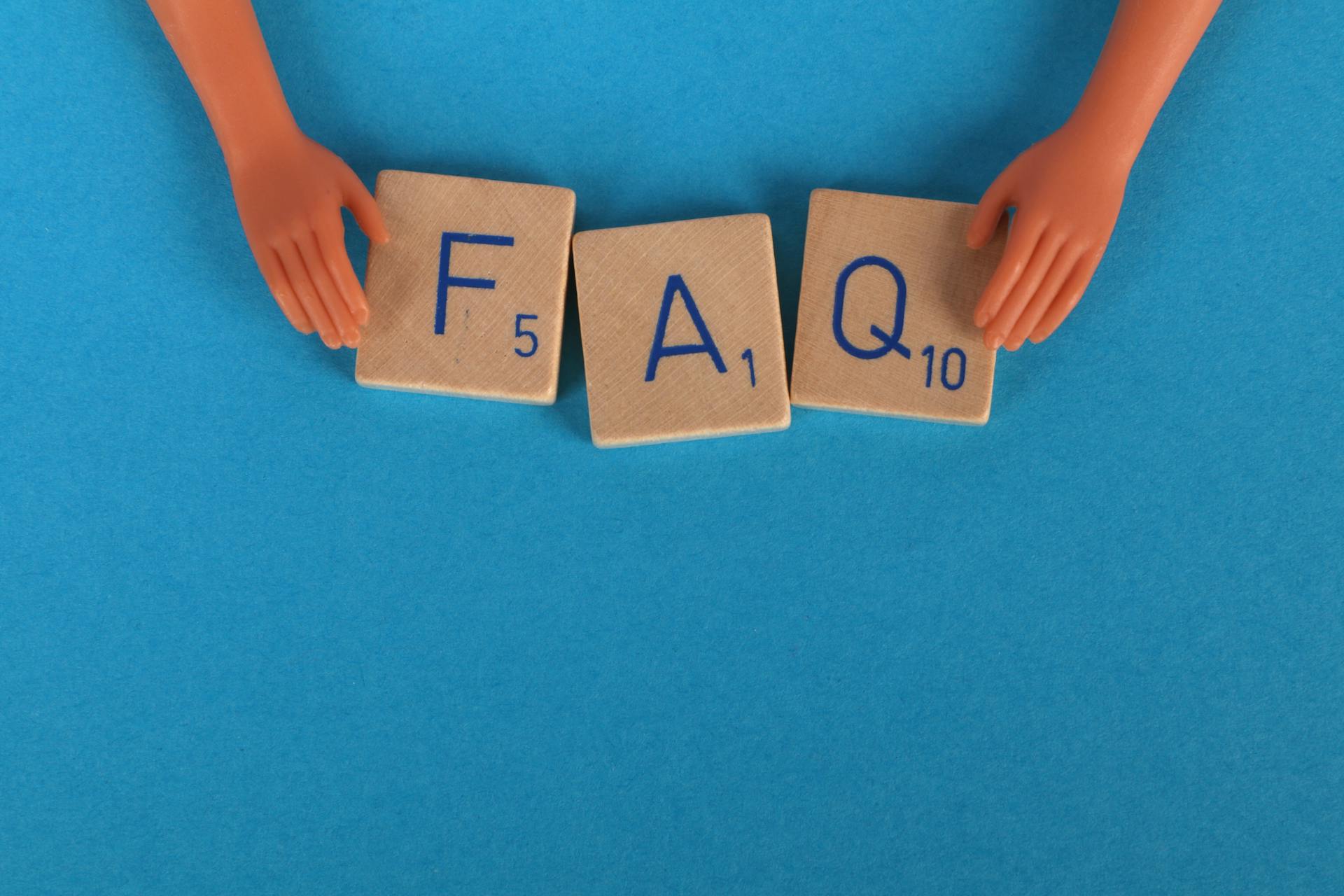 Wooden letter tiles spelling "FAQ" with toy hands on a blue background.