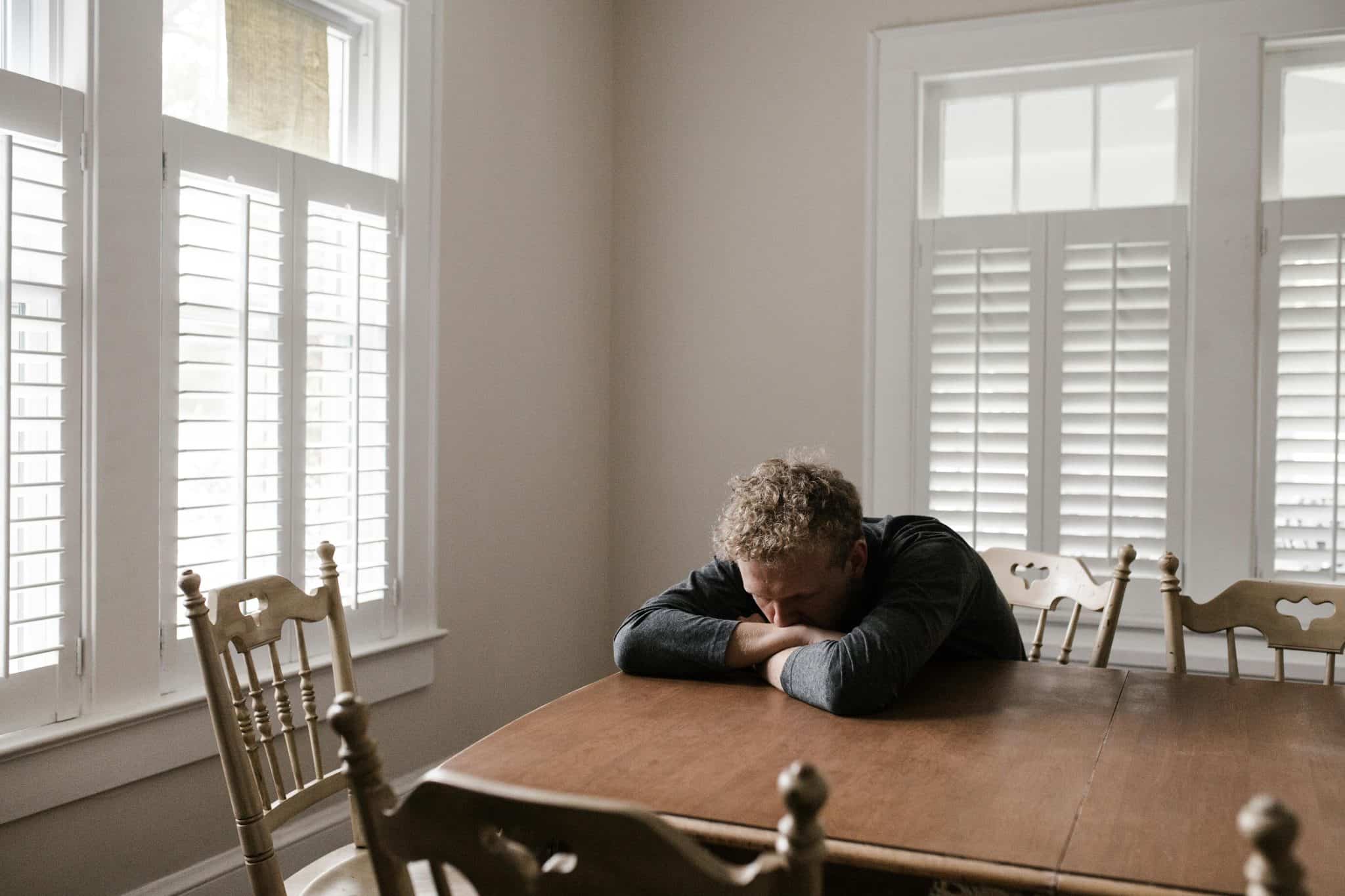 Man resting his head on a table in a bright room, appearing exhausted and anxious possible causes of bruxism