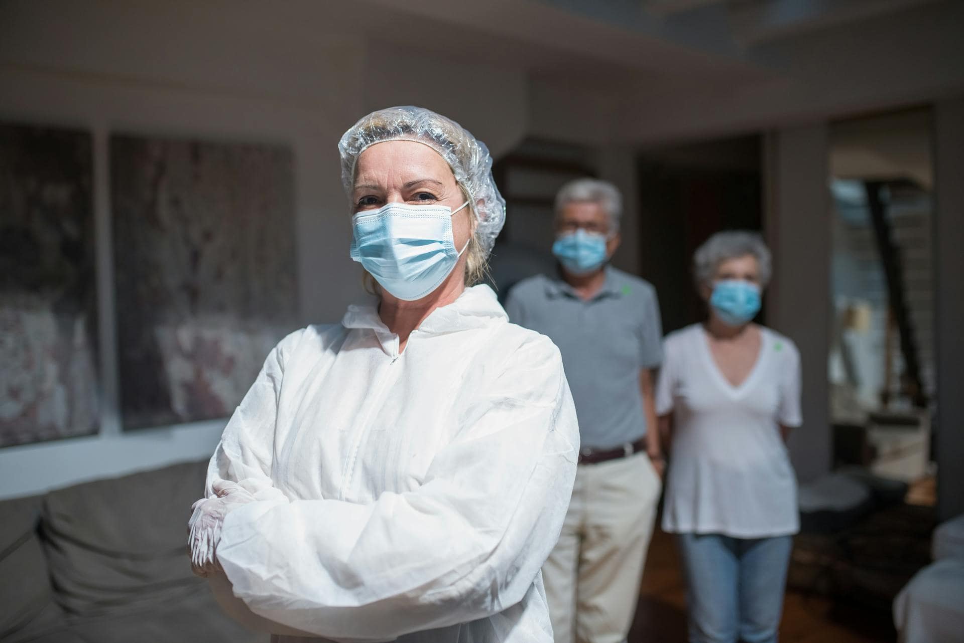 Frontline healthcare worker in protective gear and face mask standing confidently in front of her family at home during the pandemic. Hypnotherapy.