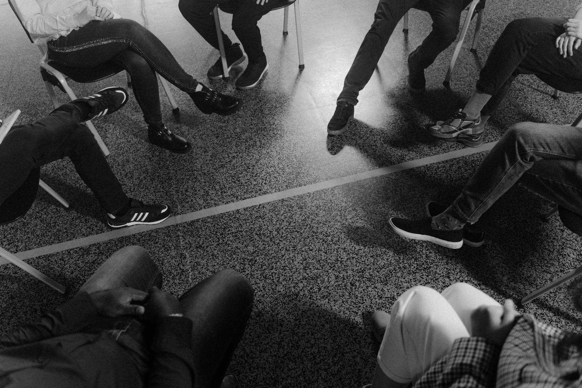 Black and white photo of people sitting in a circle during a group therapy or support session.