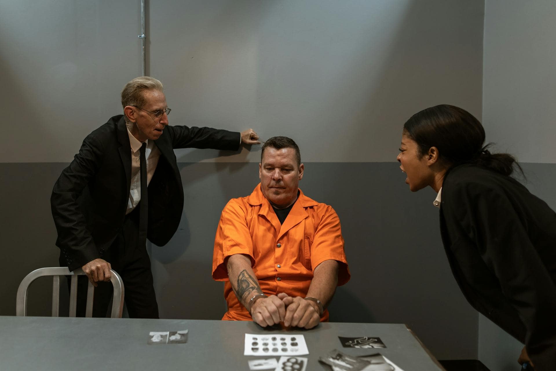 An inmate sits in a dimly lit interrogation room, showing visible signs of stress or anxiety, possibly during questioning by authorities.