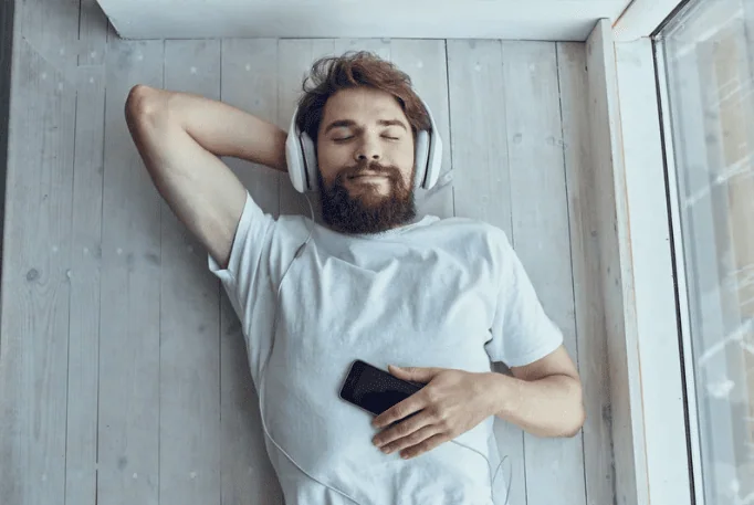 Man lying back with headphones and a phone, about to press play