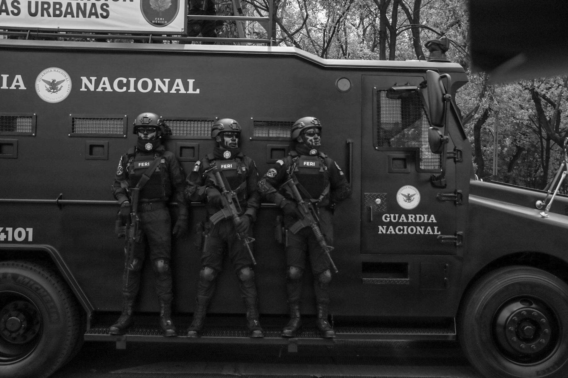 Armed national guard officers standing on a tactical armored vehicle, prepared for urban operations and high-risk environments.