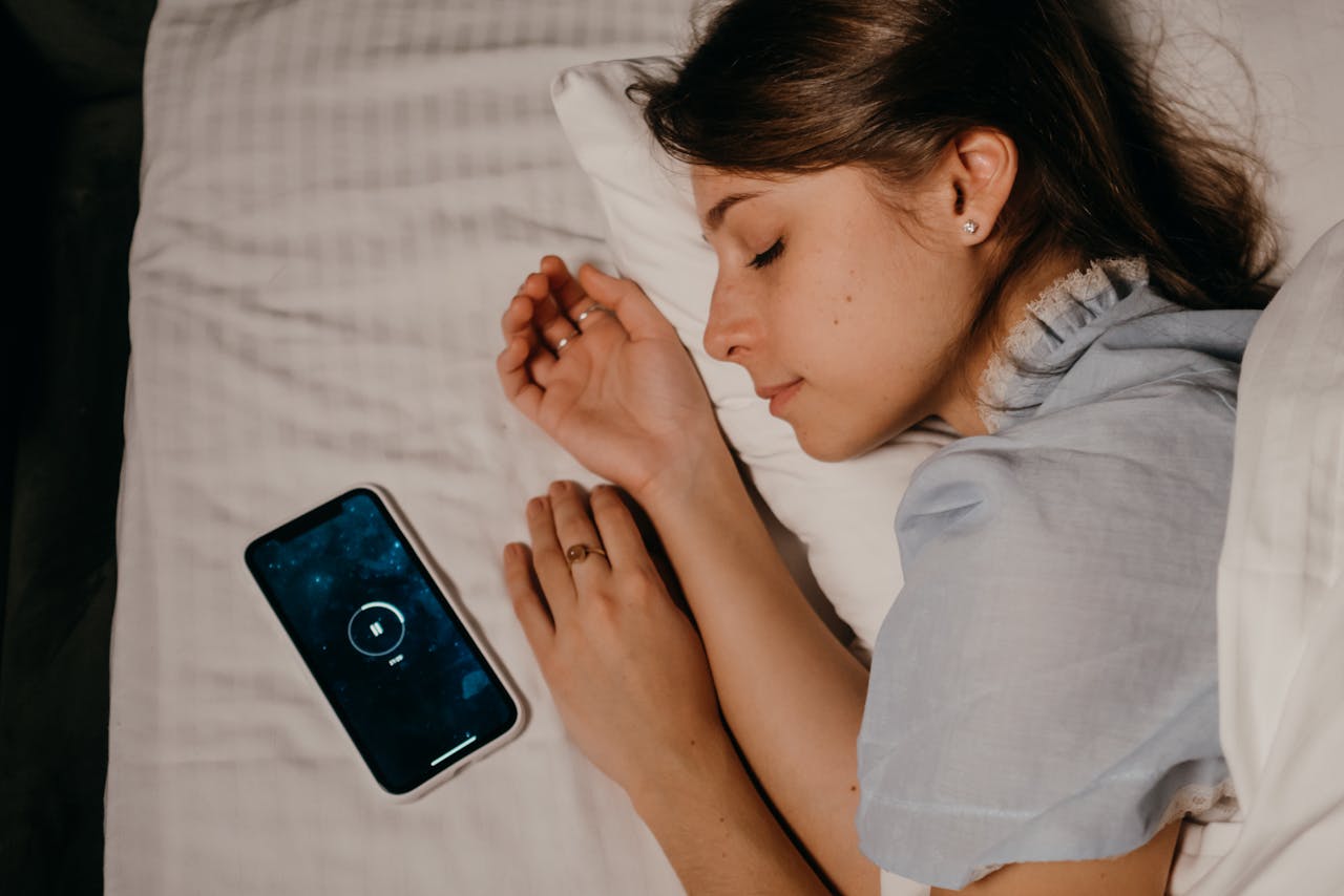 Hypnotherapy for sleep: A woman peacefully sleeping on a bed while listening to a guided hypnosis session on her smartphone.