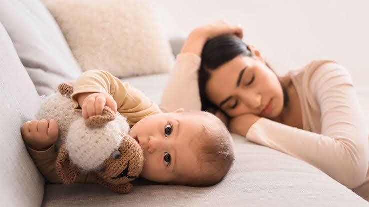 Mother resting on the bed beside her baby