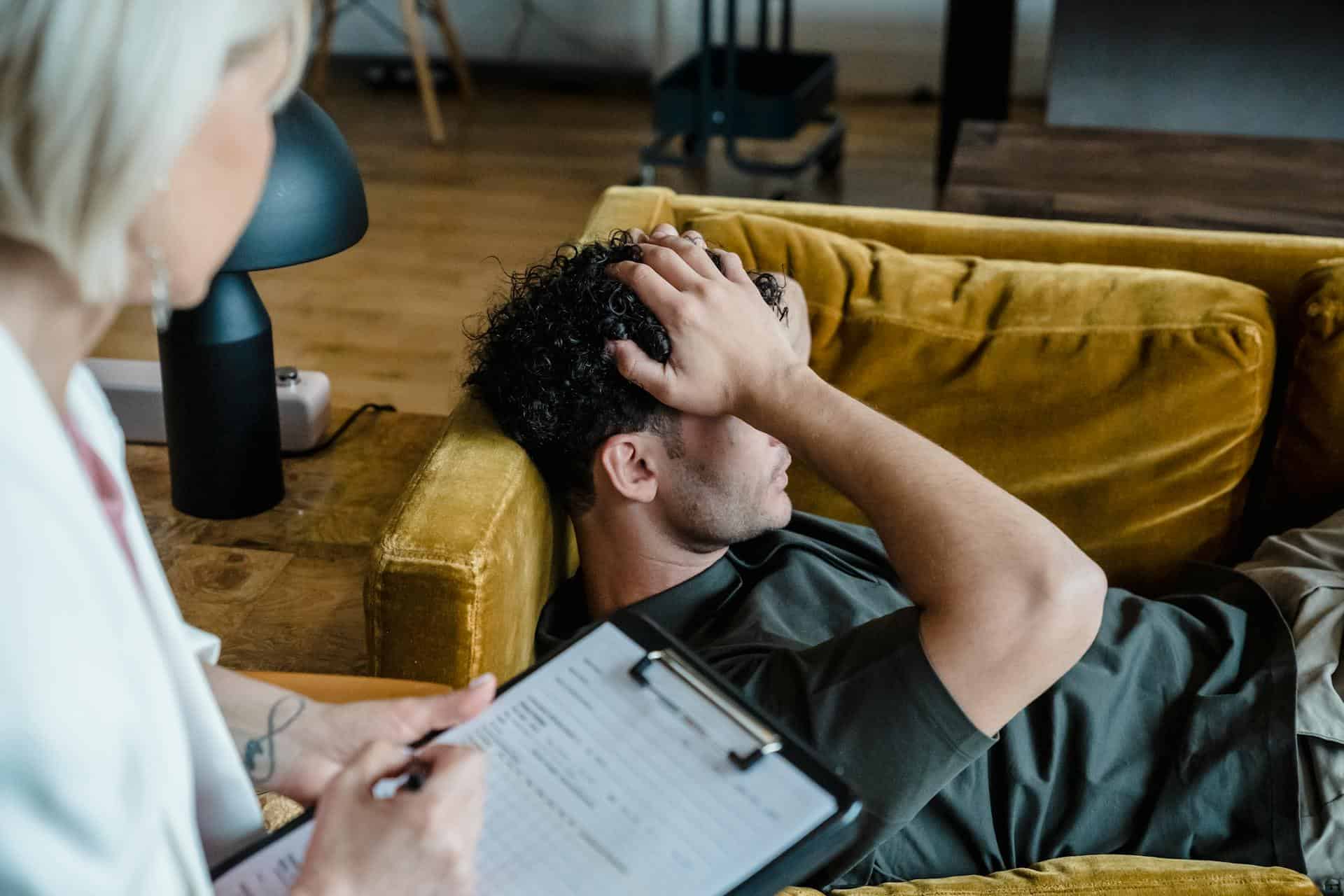 A man lying on a sofa with a distressed expression during a therapy session, symbolizing emotional support through hypnotherapy.