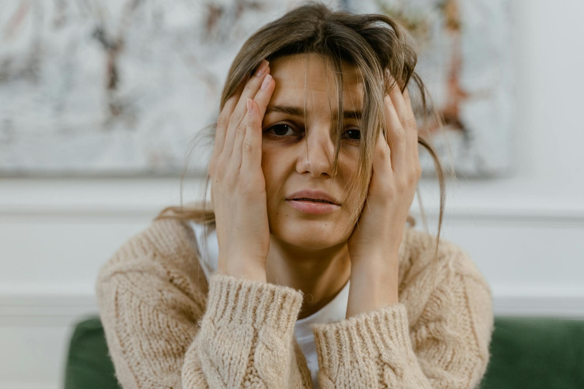 Young woman with a tired expression holding her head in her hands, showing signs of stress, fatigue, or emotional overwhelm.