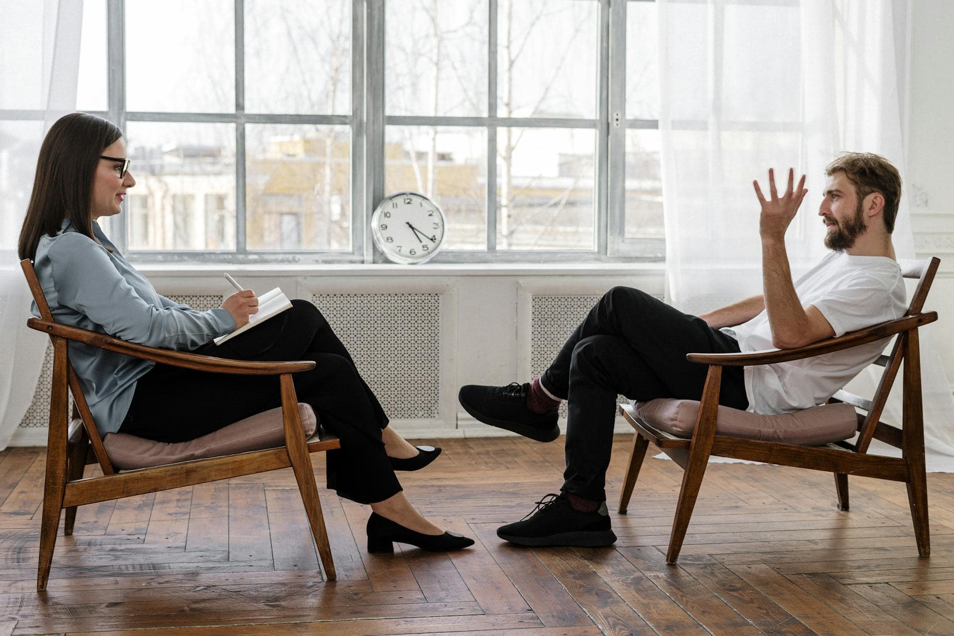 Male client speaking with a female therapist during a counselling session in a bright, modern office setting.