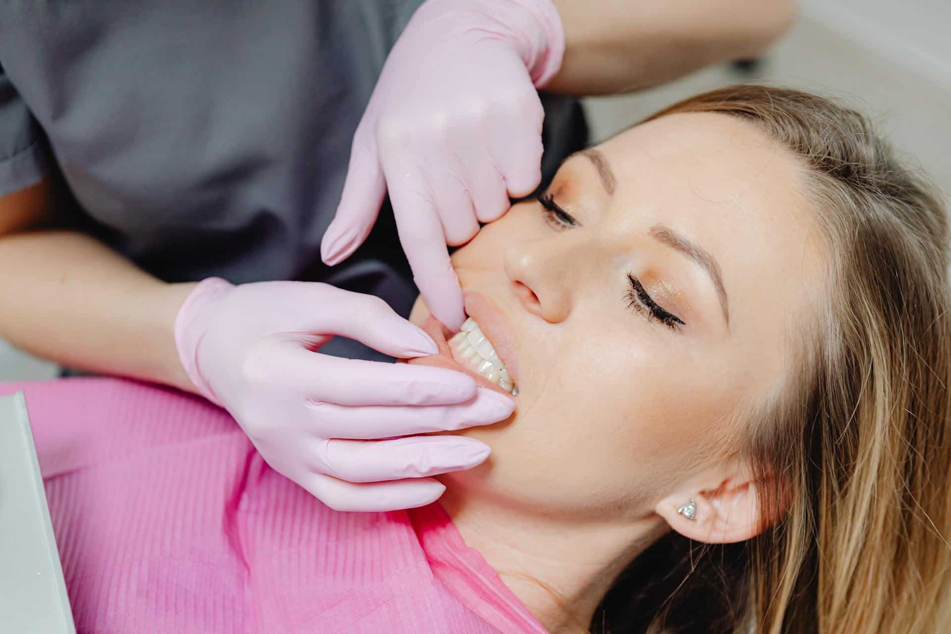 A woman receiving a dental examination with pink-gloved hands checking her jaw and bite alignment, commonly part of TMJ disorder evaluation.