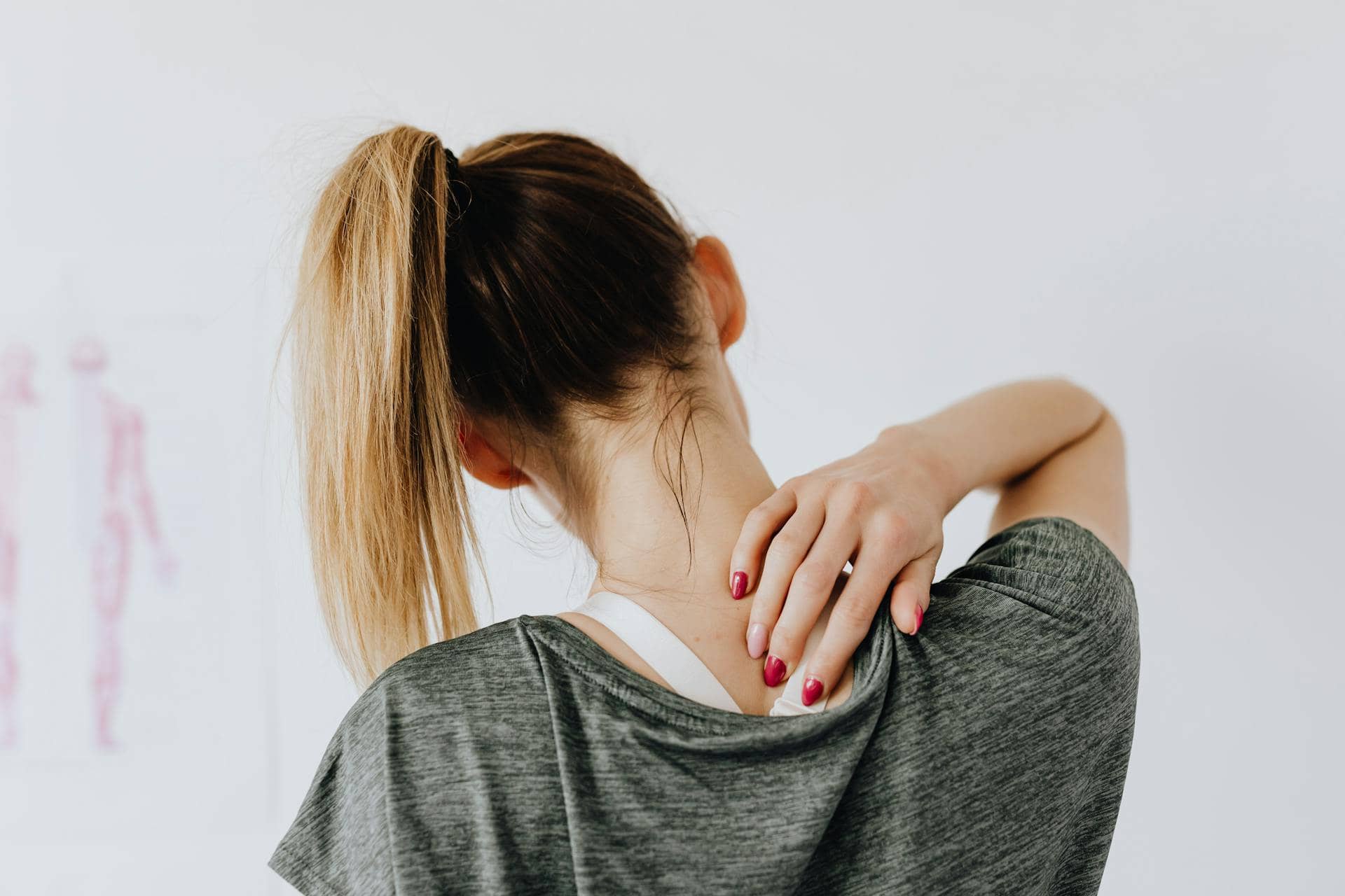 Woman with a ponytail touching her neck, indicating discomfort or muscle pain.