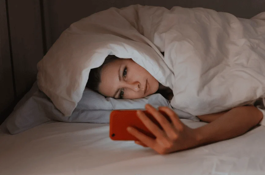Woman on her phone in bed with her mind still planning